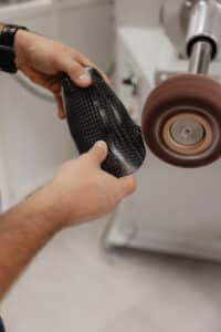 Fabrication d'une prothèse : mains façonnant un manchon en fibre de carbone sur une machine de finition rotative.