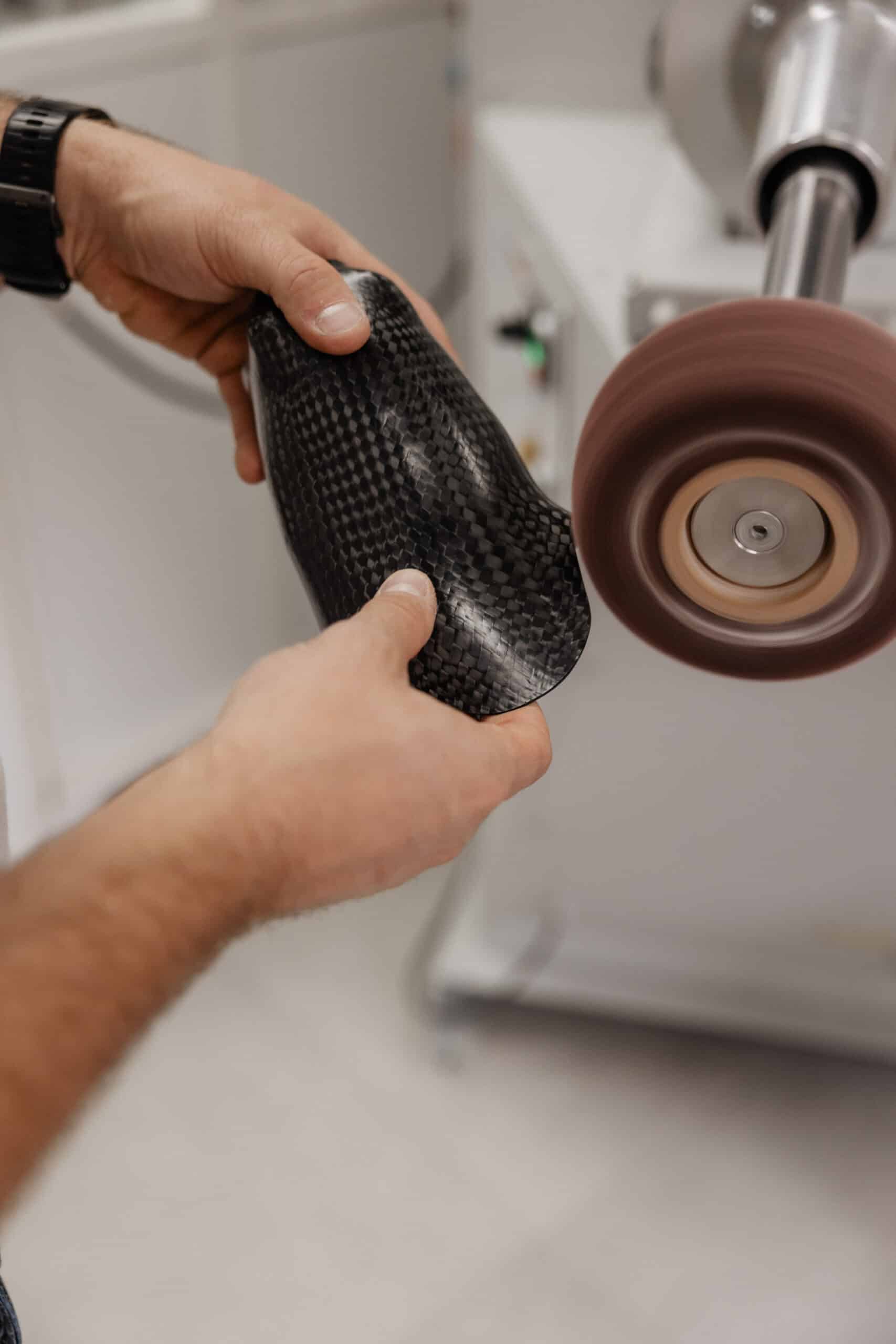 Fabrication d'une prothèse : mains façonnant un manchon en fibre de carbone sur une machine de finition rotative.