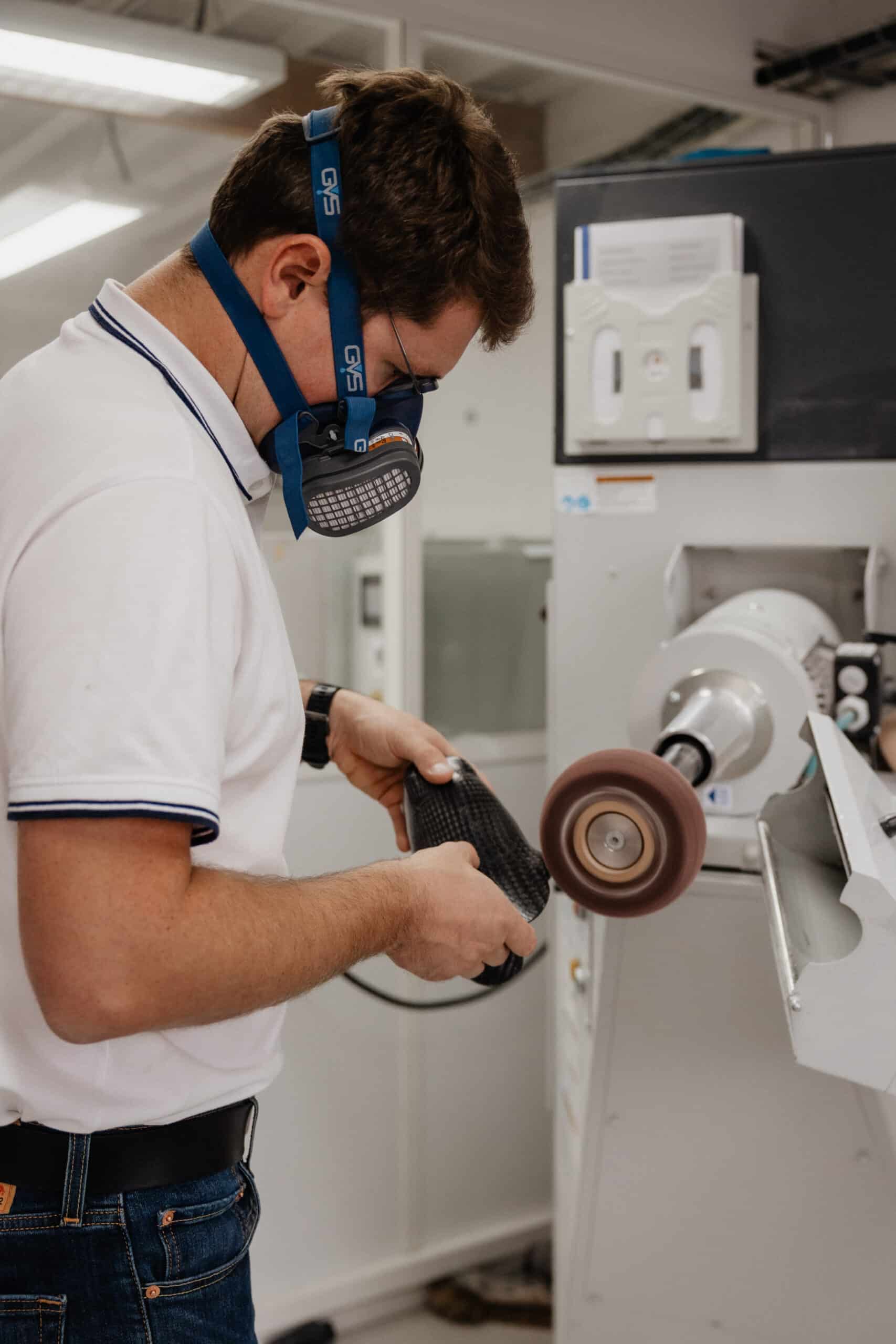 Technicien portant un masque respiratoire GVS polissant une prothèse en fibre de carbone sur une meuleuse.