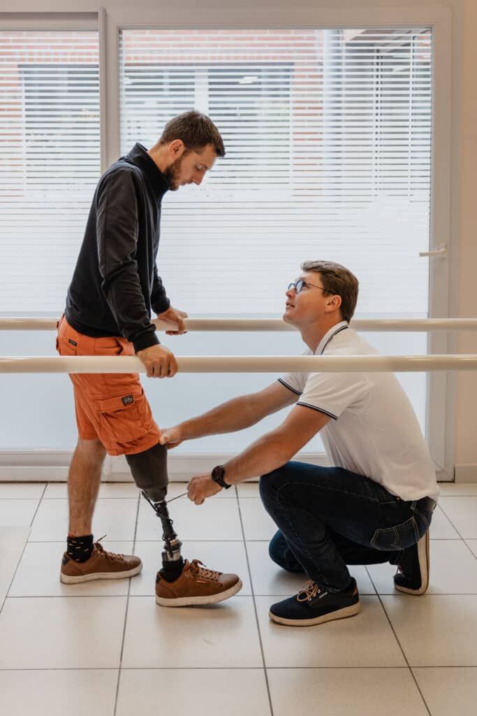 Ajustement précis de prothèse de jambe pour la rééducation. Orthoprothésiste ajustant la prothèse de jambe d'un patient debout (amputation transtibiale), utilisant les barres parallèles en rééducation.