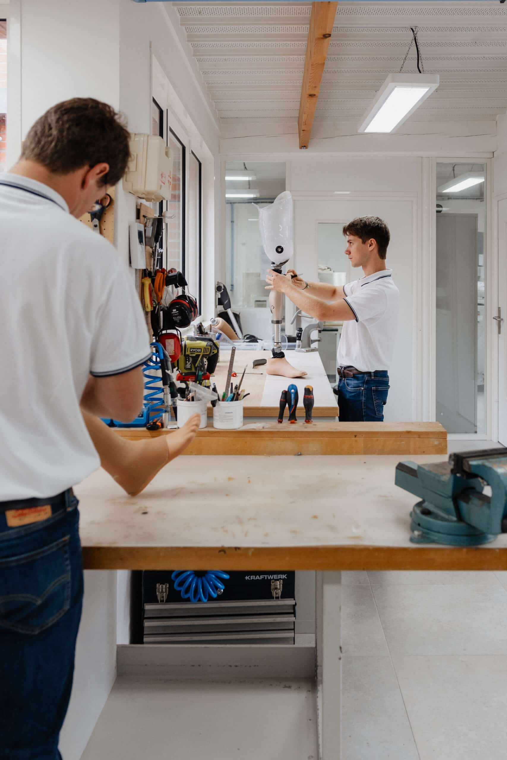 Prothésiste ajustant une jambe artificielle (prothèse transtibiale) sur un établi d'atelier. Outils, lumière vive et environnement propre.