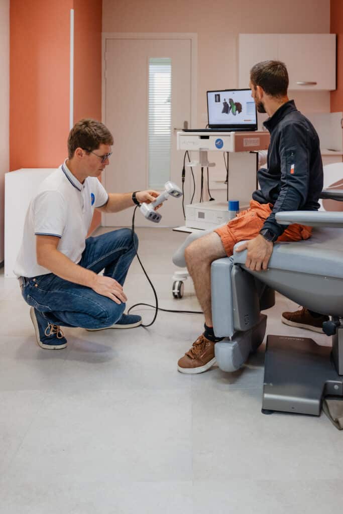 Professionnel de santé utilise un scanner 3D (Peel 3D) pour la mesure numérique de la jambe d'un patient assis. Écran Vytruve visible. Professionnel de santé utilise un scanner 3D (Peel 3D) pour la mesure numérique de la jambe d'un patient assis. Écran Vytruve visible.