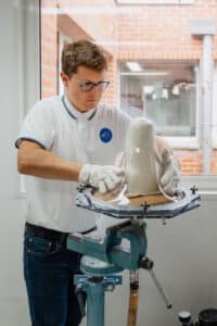 Technicien en gants blancs réalisant le thermoformage d'un moule pour prothèse ou orthèse sur un établi. Logo EPF sur son polo blanc.